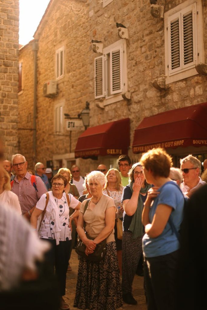 A diverse group of tourists walks through a historic city street with stone buildings.